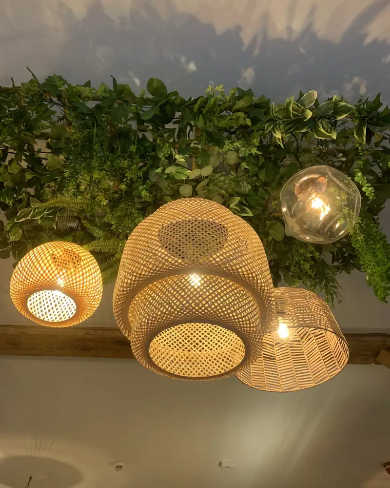 Wiklinowe lampy nad stołami i ściana z zieleni